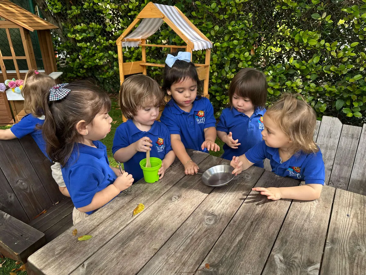 Four children in blue Bufi polos playing together at a wooden picnic table under the playhouse