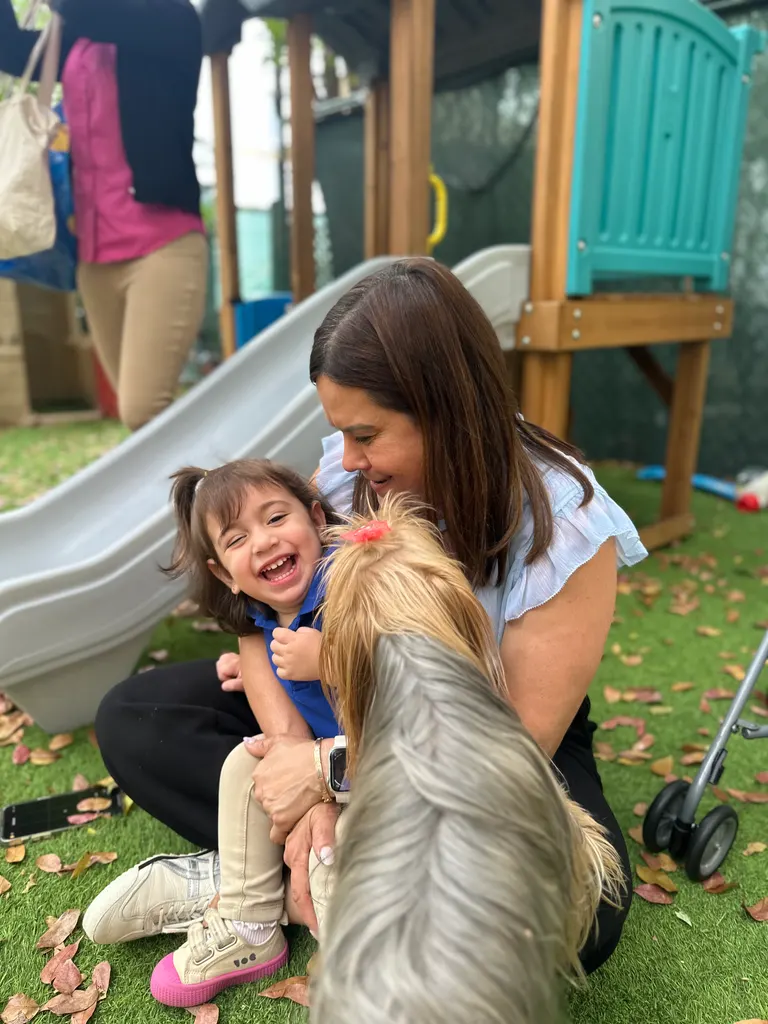 A teacher kneeling in the garden, hugging a laughing child