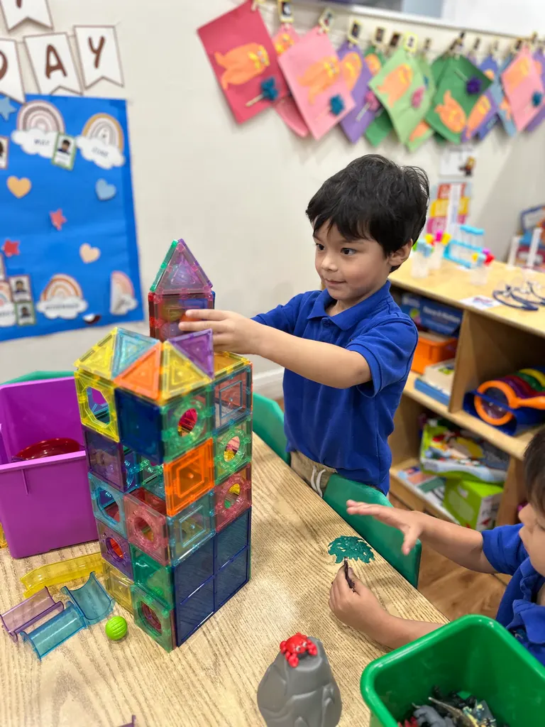 A boy stacking a tall tower of magnetic tiles in the classroom
